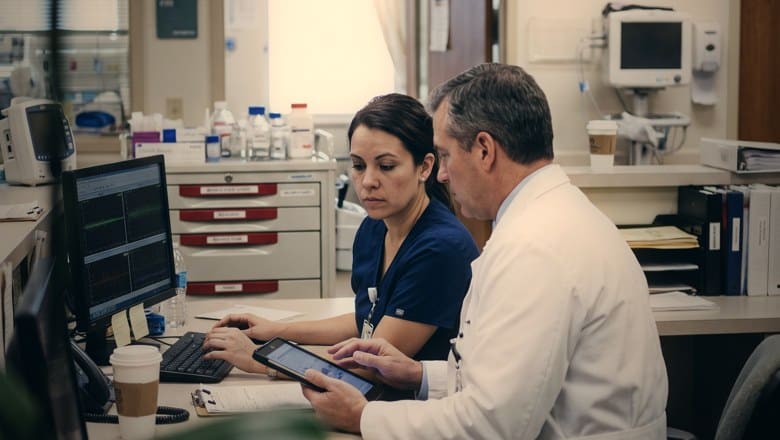 A nurse and a doctor reviewing a patient chart on a tablet at a ward station